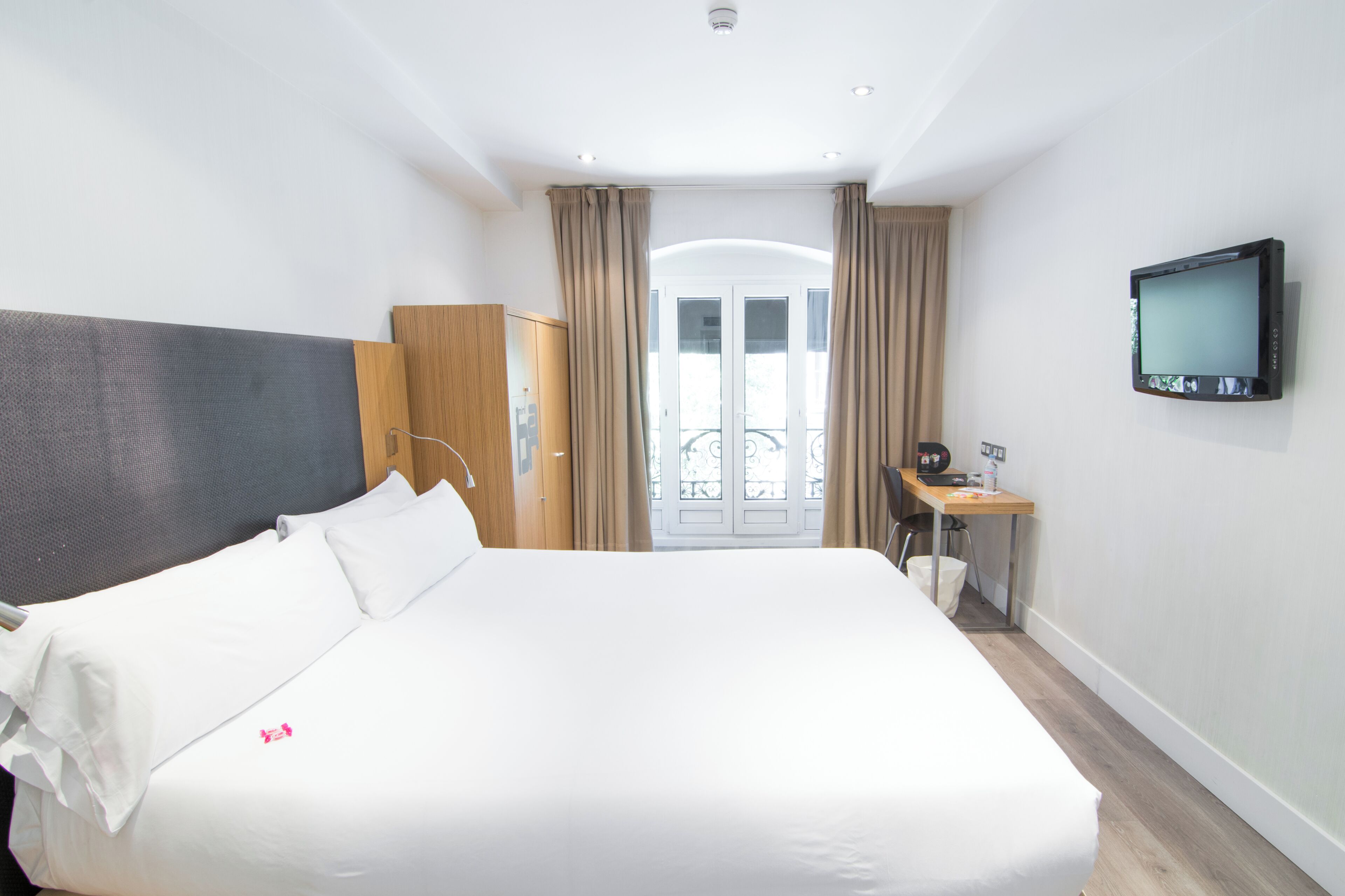 A hotel room with a large bed, a desk with a chair, a television, and a wardrobe.