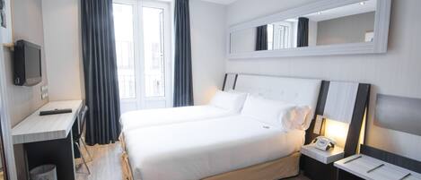 Habitación de hotel con cama, mesita de noche, lámpara, televisor y escritorio con silla.