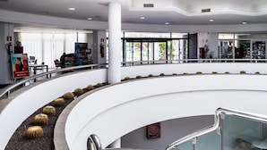 A modern interior with a central glass dome, a curved staircase, and a lower level with a cactus garden. - Hotel BlueBay Lanzarote - All inclusive (Teguise)