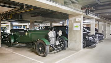 A parking garage with multiple cars, including a vintage green car and a modern black car.