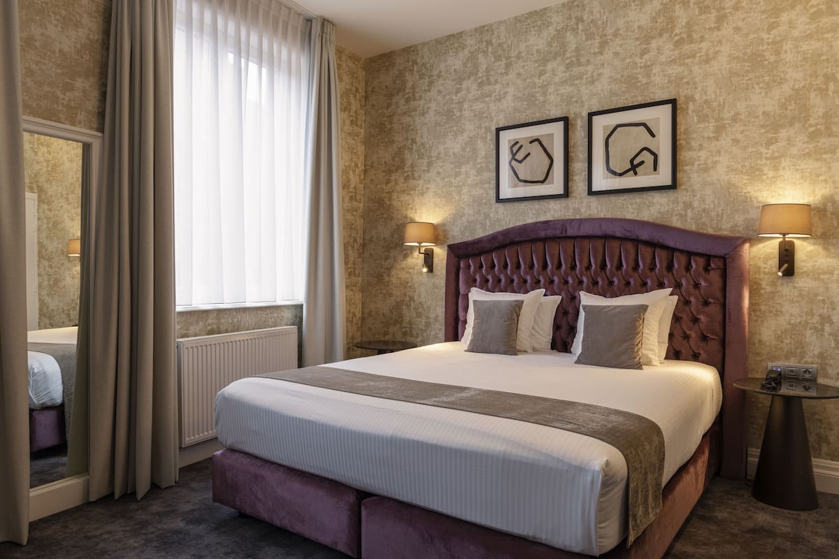 Ein Hotelzimmer mit einem großen Bett, zwei Nachttischlampen, einem Spiegel und einem mit Vorhängen versehenen Fenster.
