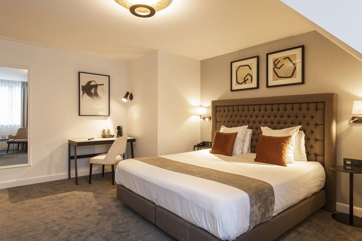 Ein Hotelzimmer mit einem großen Bett, einem Schreibtisch und einem Stuhl. Über dem Bett hängen zwei gerahmte Bilder an der Wand.