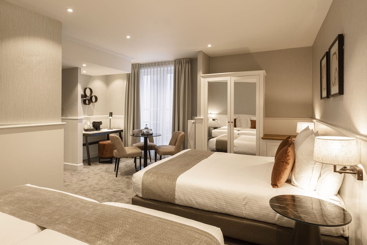 Ein Hotelzimmer mit einem großen Bett, einem Schreibtisch mit Stühlen, einem kleinen Tisch und Blick ins Freie durch ein Fenster.