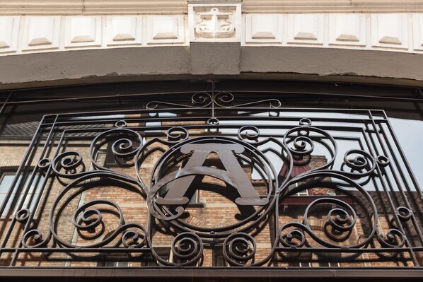 A wrought iron gate with a large 'A' emblem, part of a building's entrance. - Dukes’ Academie – by Dukes’ Hotel Collection (Bruges)