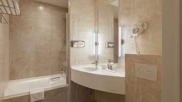 A modern bathroom with a bathtub, a large mirror, a hairdryer, and a towel rack.