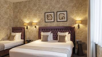 A hotel room with two beds, a large headboard, wall-mounted lamps, and framed artwork.