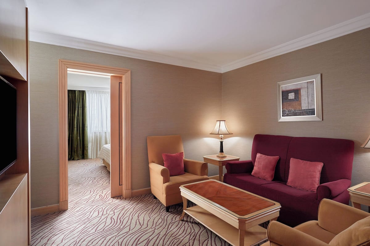A hotel room with a sofa, armchair, and a television.