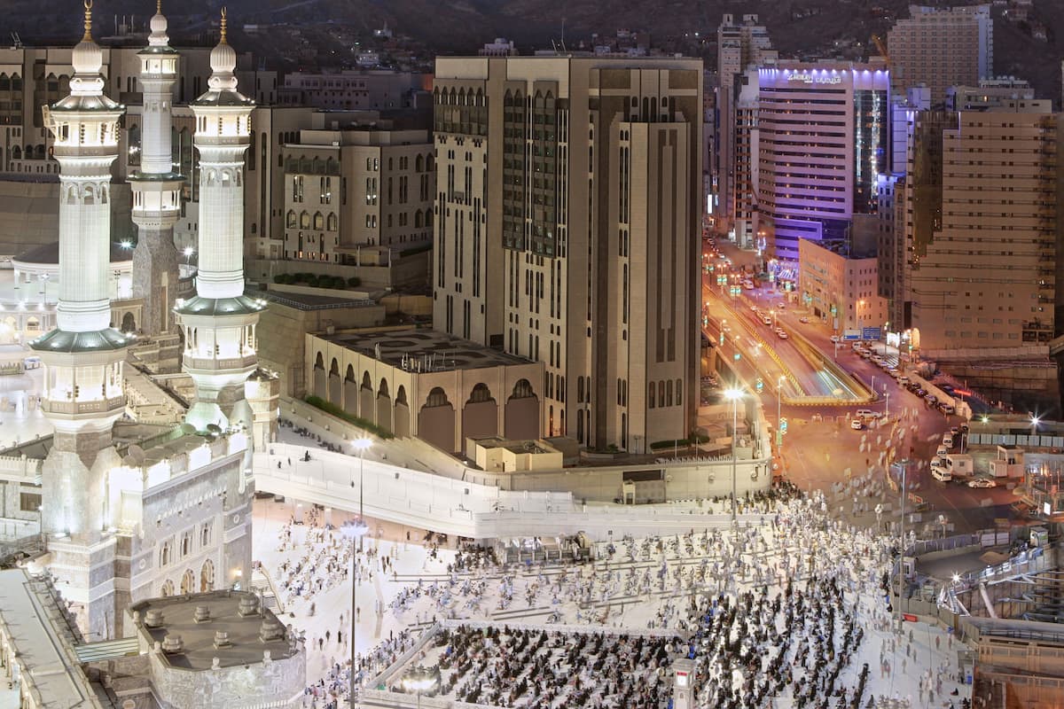 A large mosque with multiple minarets and a central courtyard filled with people.