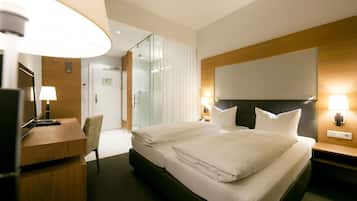 A hotel room with a large bed, a desk, a chair, a TV, and a mirror.