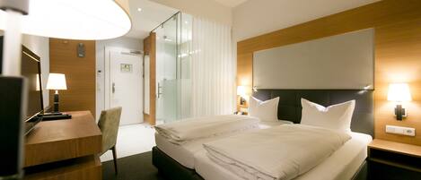 Habitación de hotel con una cama grande, un escritorio, una silla, un televisor y un espejo.