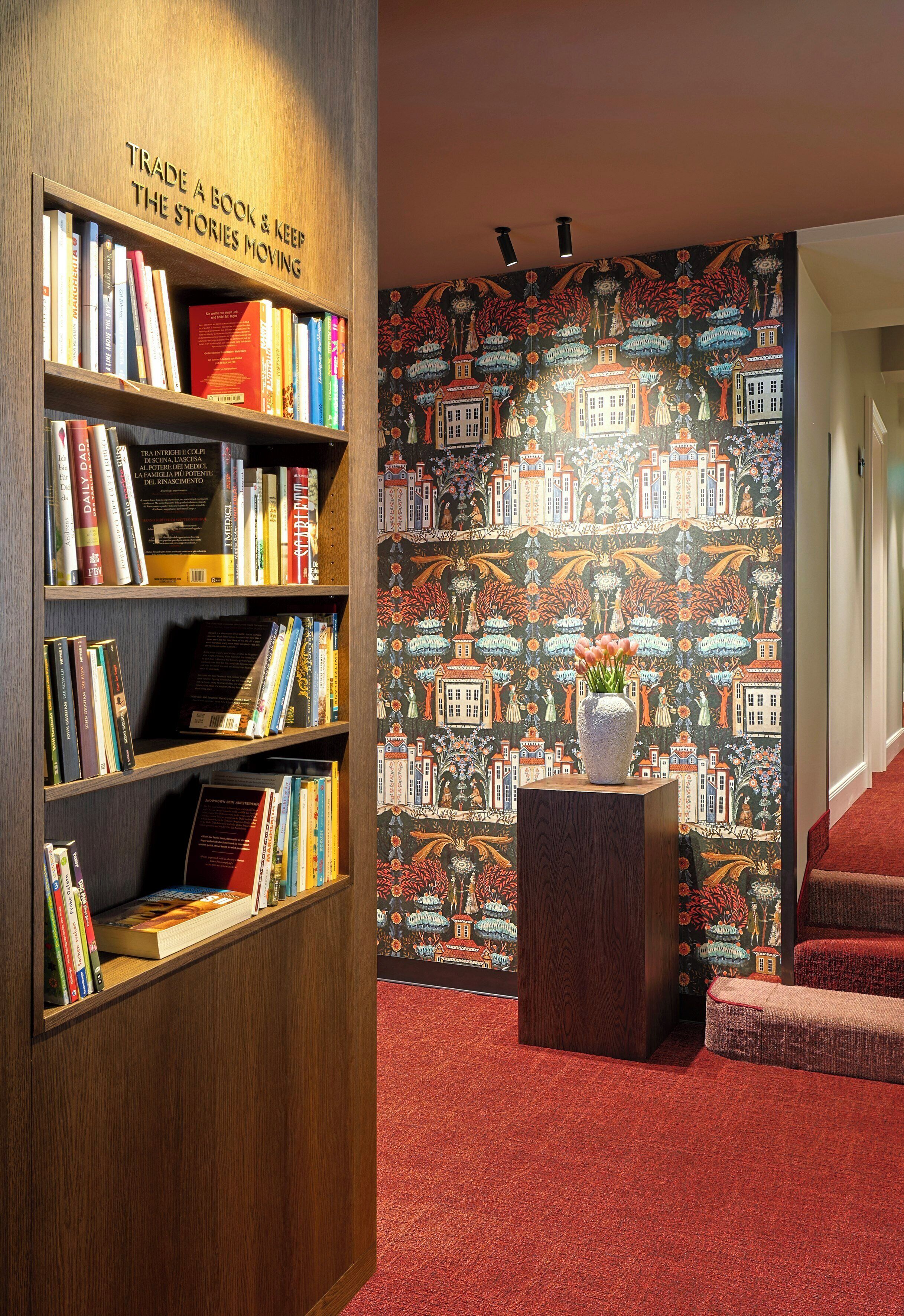 Une bibliothèque avec des étagères, un papier peint à motifs et un vase rempli de fleurs.