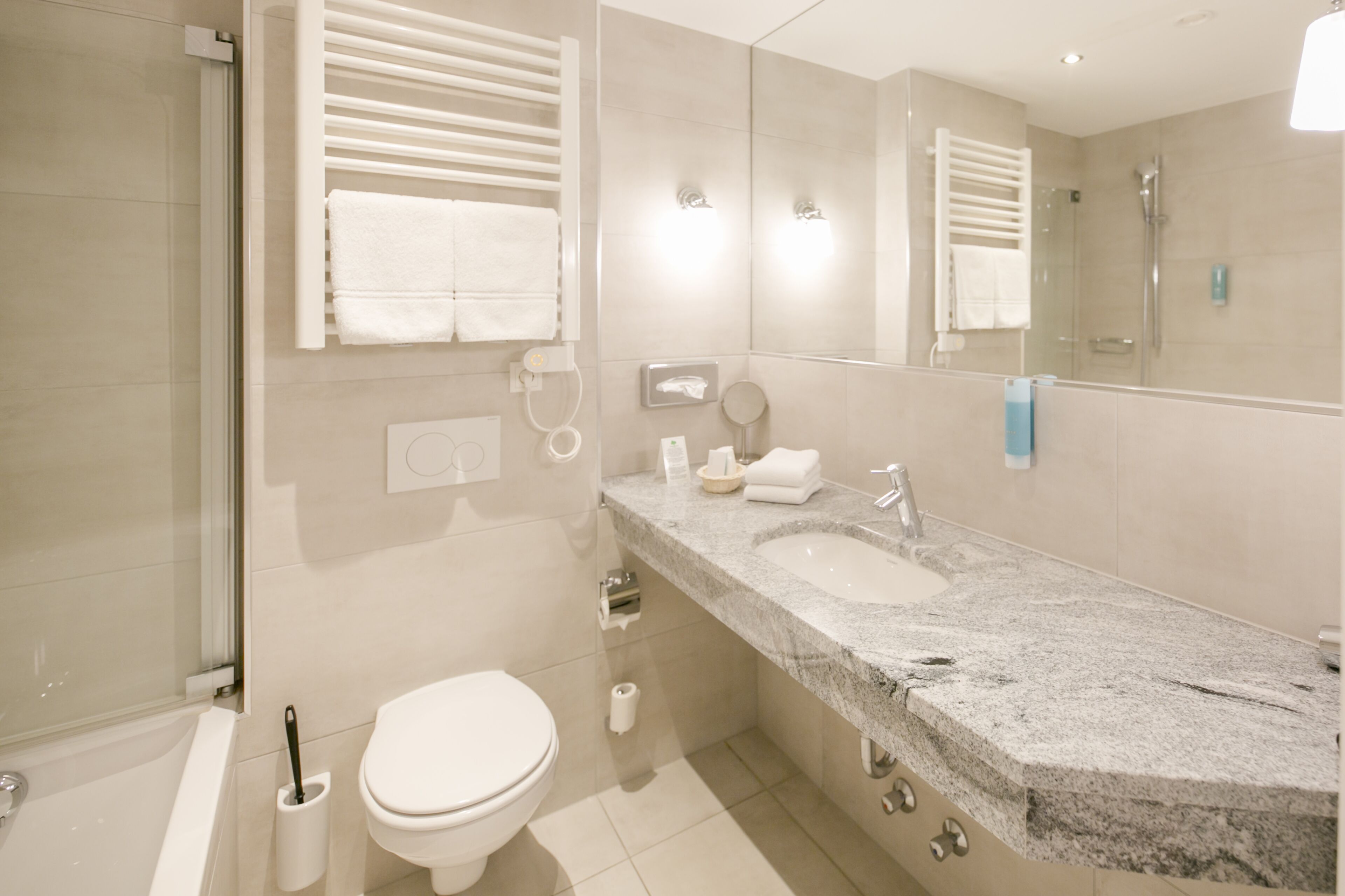 A modern bathroom with a glass shower enclosure, a white toilet, a granite countertop sink, and a large mirror.