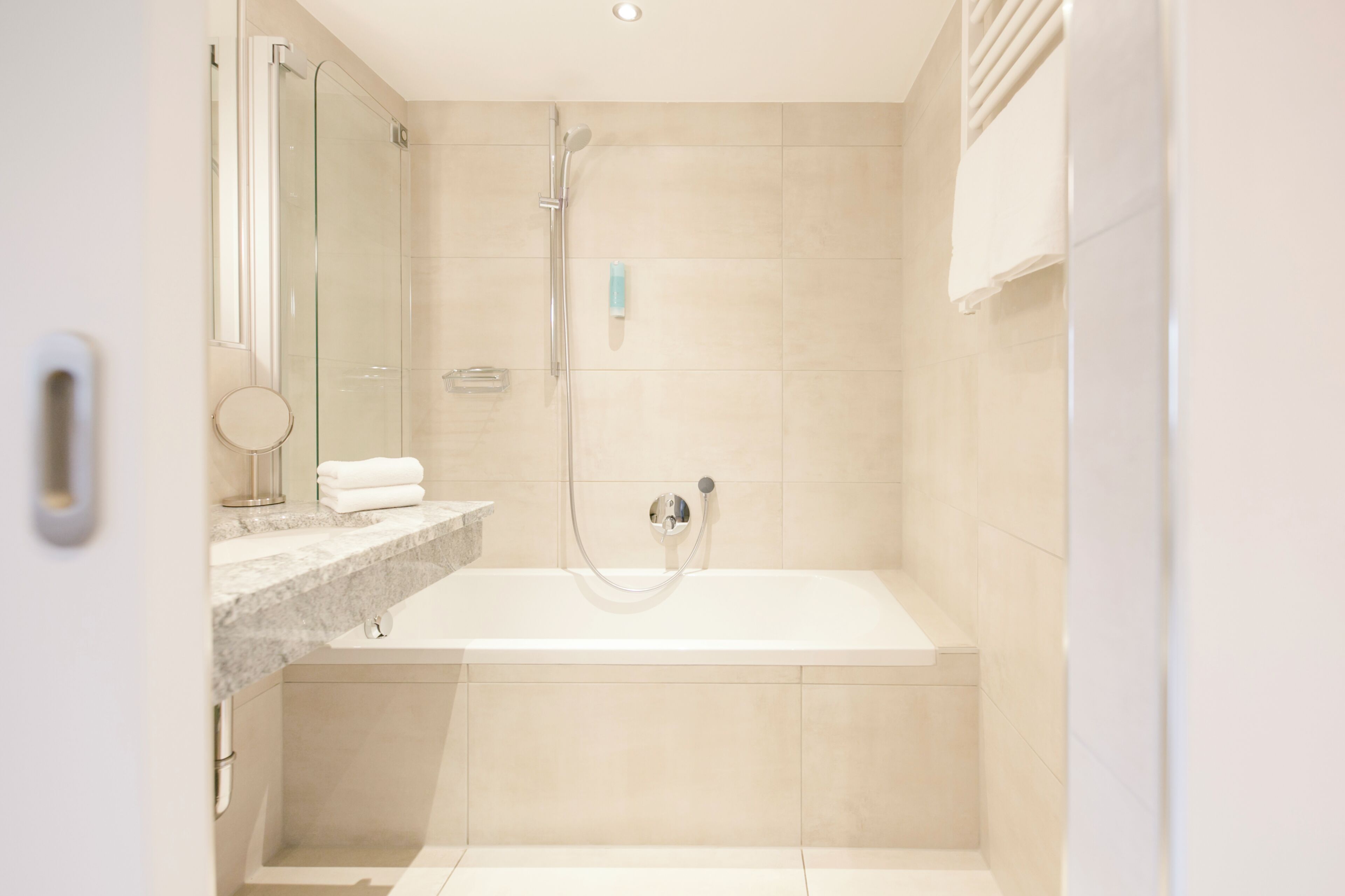 A modern bathroom with a glass shower enclosure, a bathtub, and a marble countertop.
