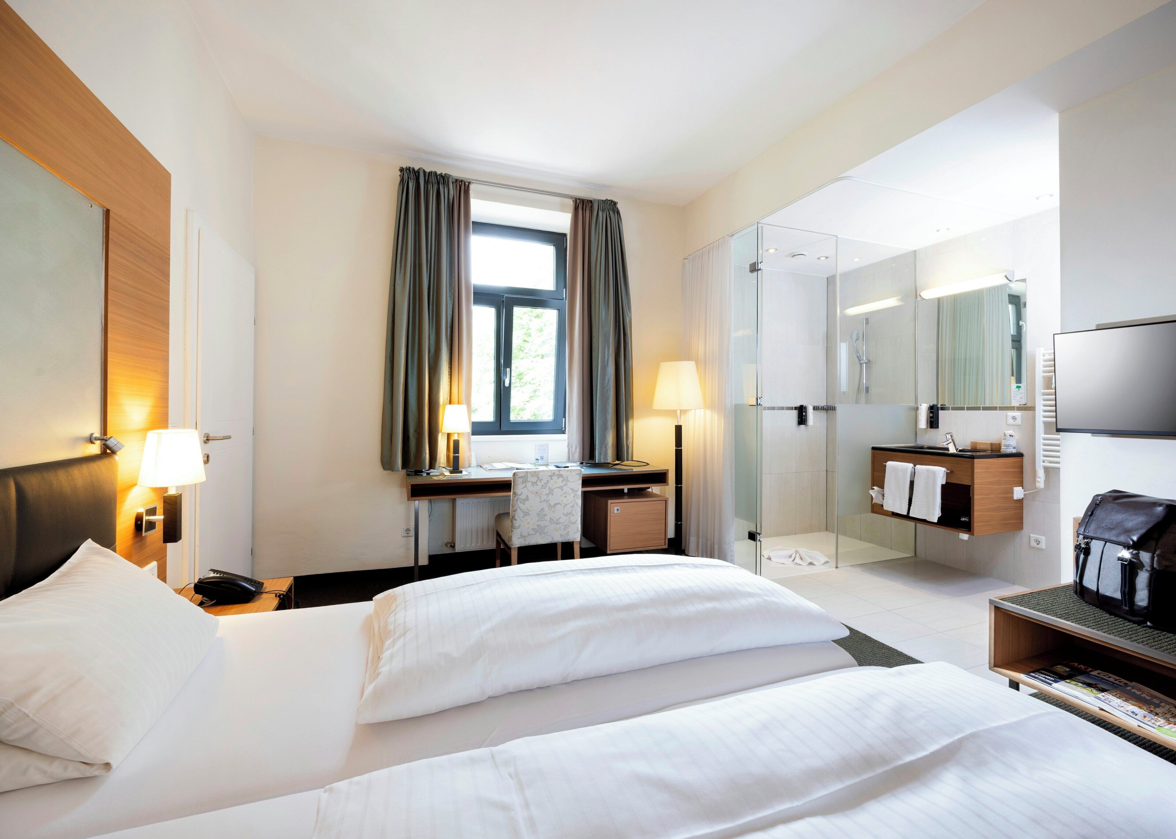 A hotel room with a bed, desk, chair, and a shower area.