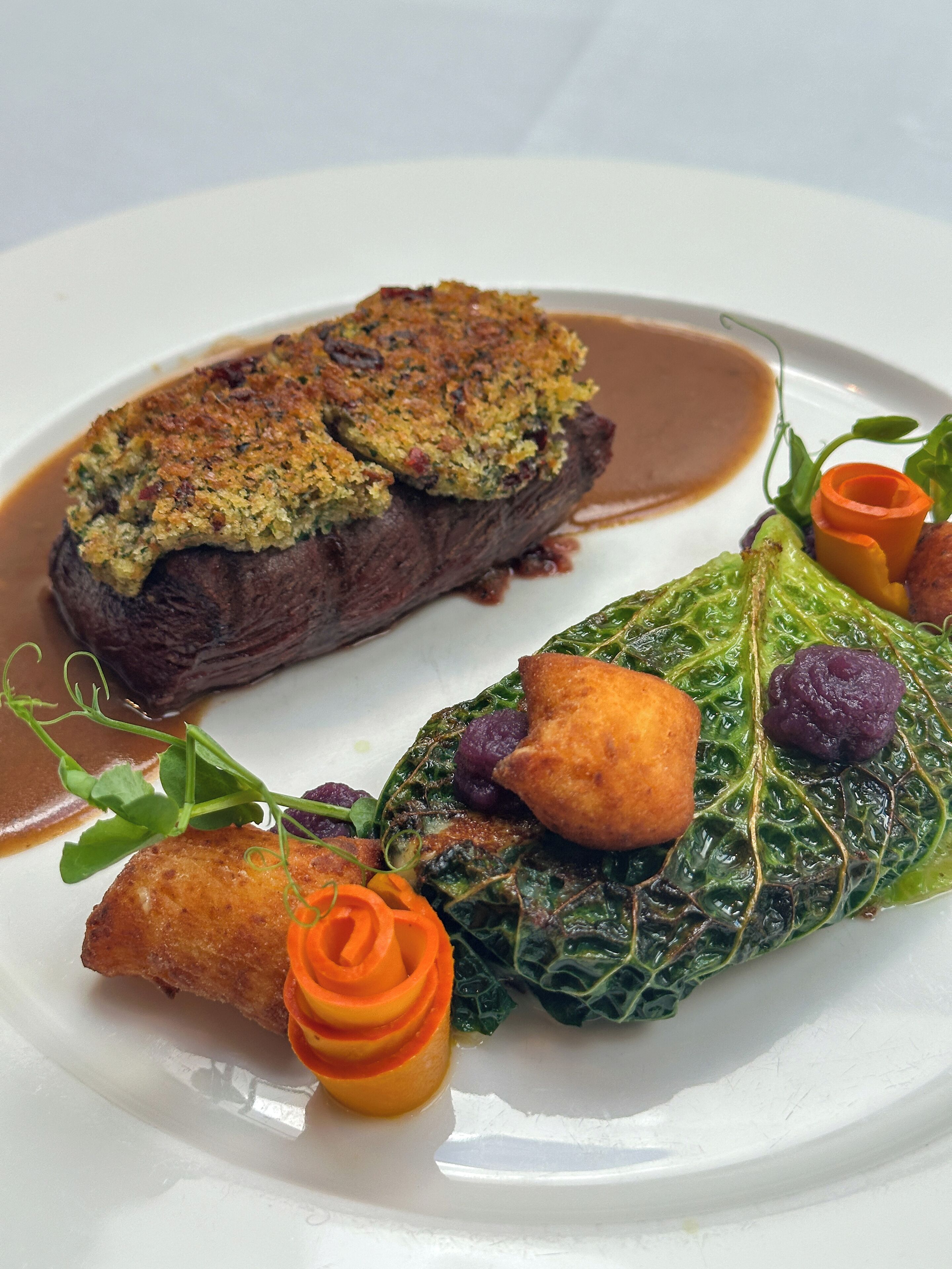 Une assiette de nourriture comprenant un morceau de viande recouvert d’une garniture croustillante, accompagné d’une portion de légumes verts et d’un petit légume orange.