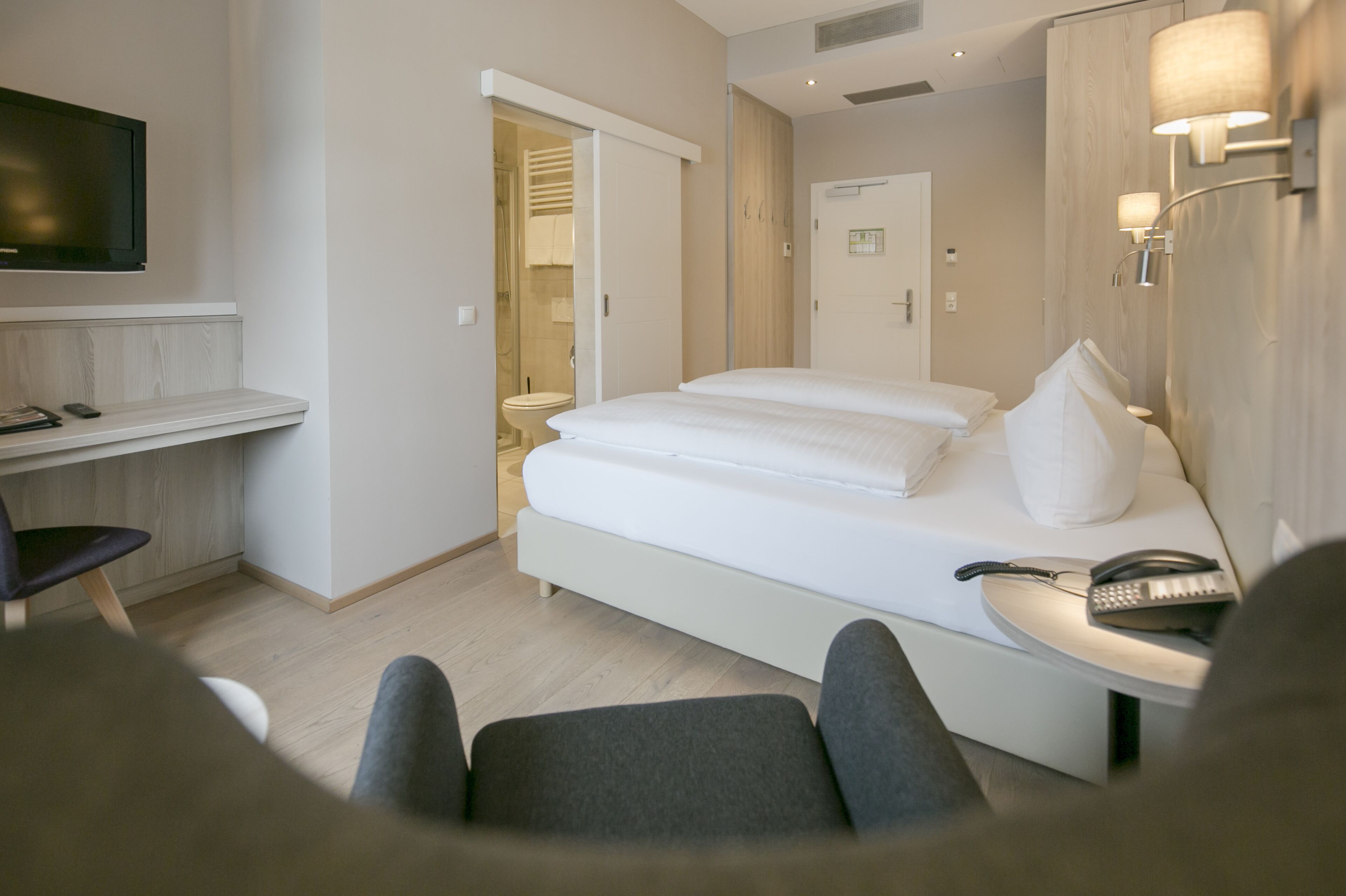 Ein Hotelzimmer mit Bett, Schreibtisch, Stuhl, Fernseher und einem durch eine offene Tür einsehbaren Badezimmer.