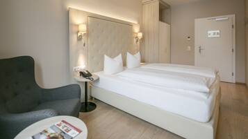 Una habitación de hotel con una cama grande, un sillón gris, una pequeña mesa redonda y un teléfono junto a la cama.