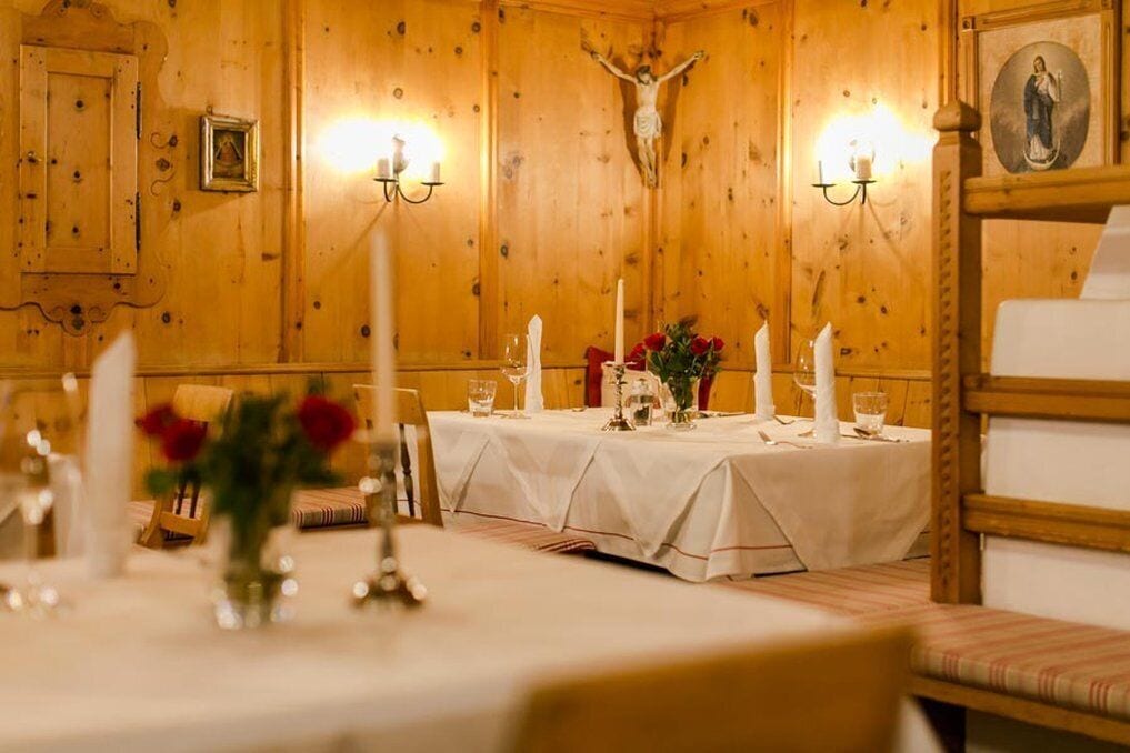 A dining area with wooden walls, a crucifix, and a table set with white tablecloths, candles, and flowers.