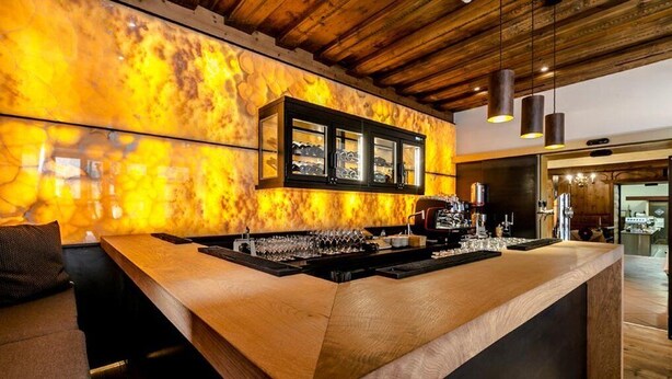 Zona de bar con mostrador de madera, enfriador de vino e iluminación colgante.