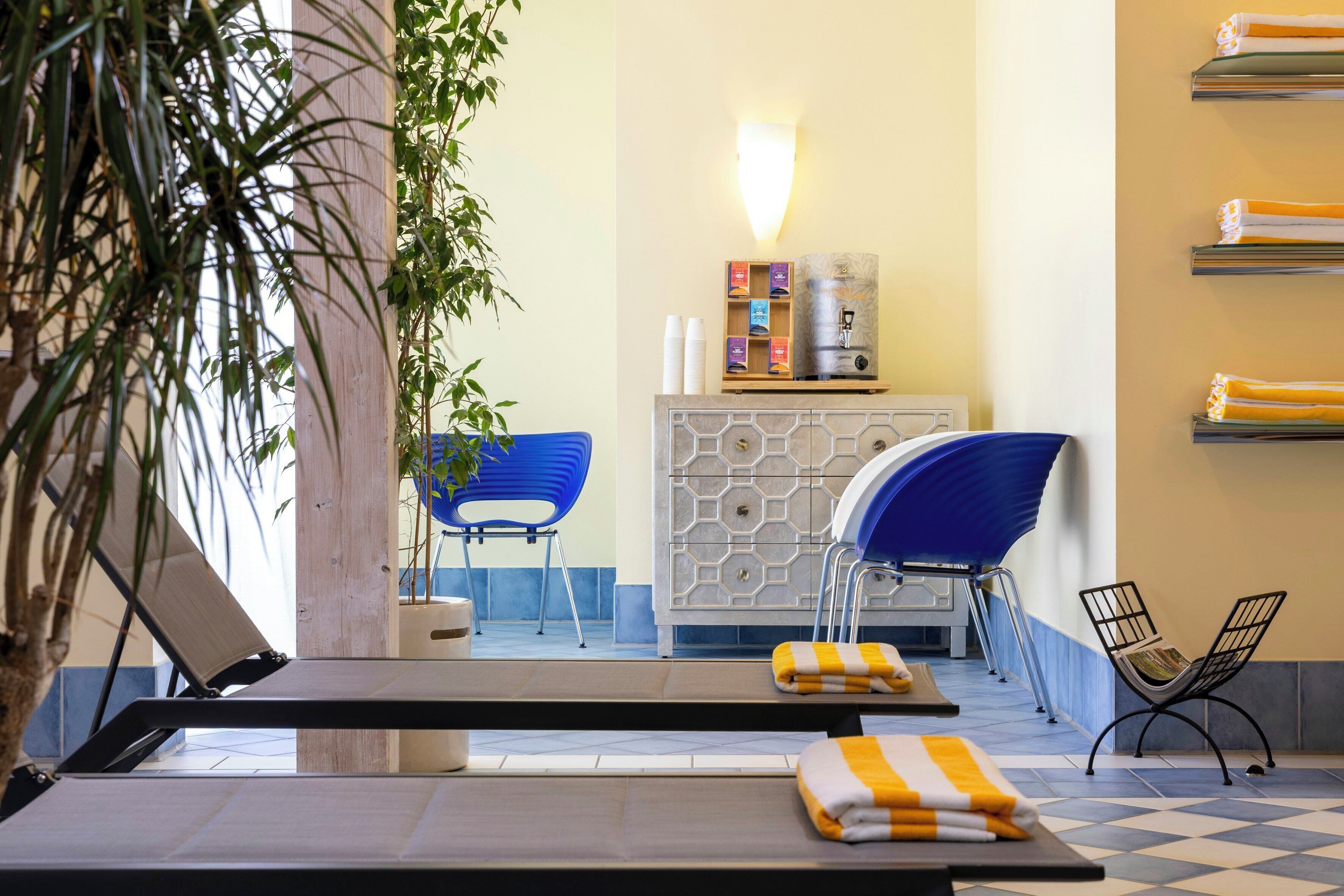 Une chambre d’hôtel avec un espace piscine comprenant des chaises longues, une chaise bleue et un meuble contenant des articles de toilette.
