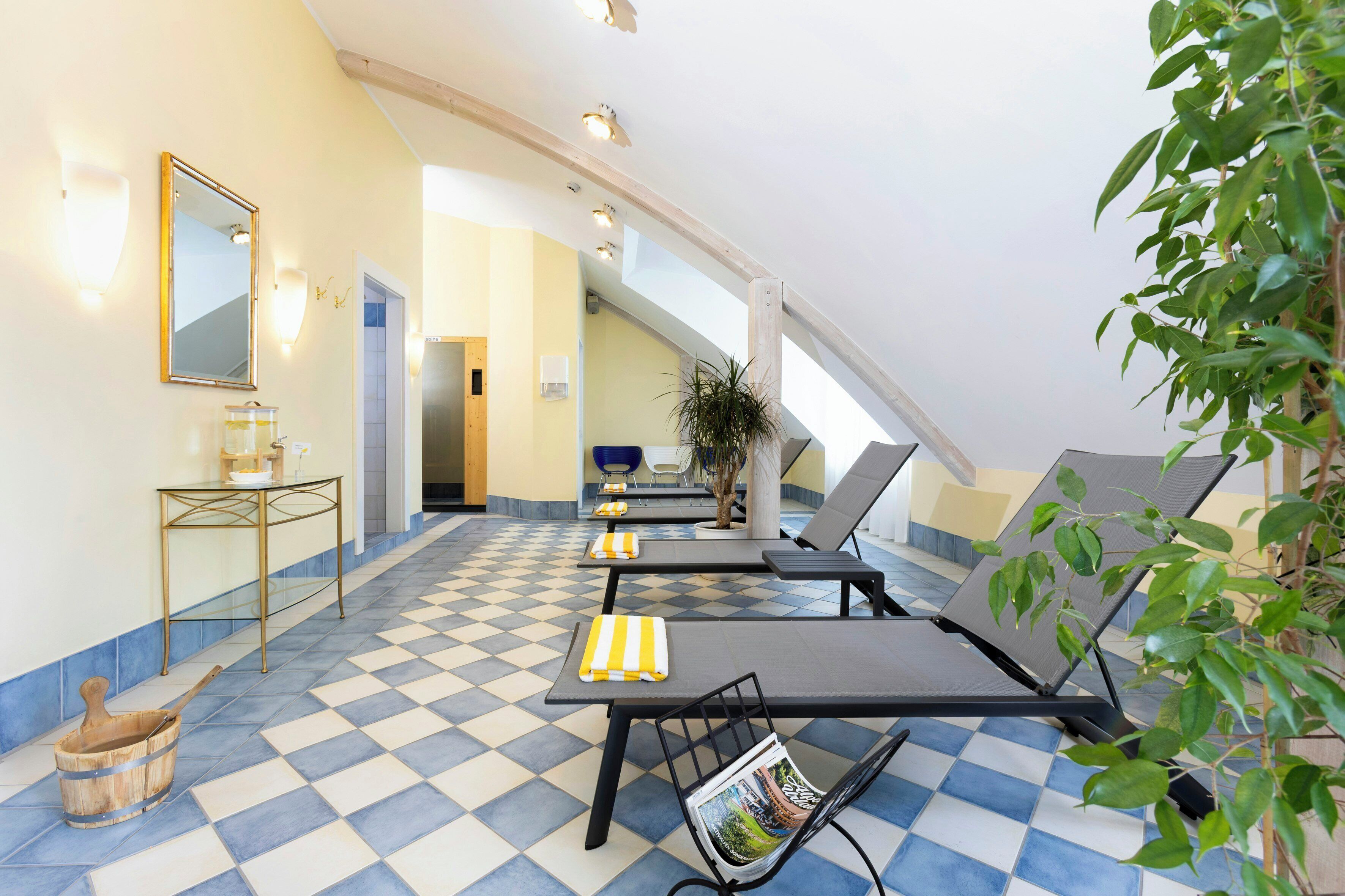 A sunlit indoor space with checkered flooring, lounge chairs, a table with a glass container, and a mirror on the wall.