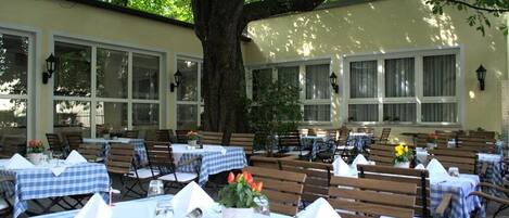 An outdoor dining area with tables set for two, surrounded by wooden benches and covered with checkered tablecloths.