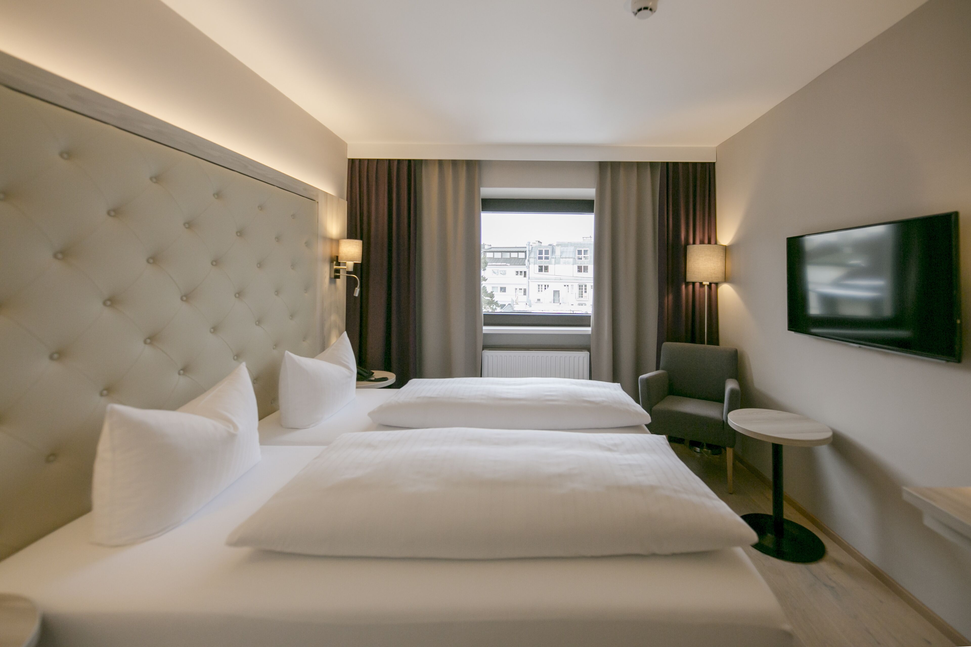 Ein Hotelzimmer mit einem großen Bett, einem Fernseher, einem Sessel und einem kleinen Tisch.