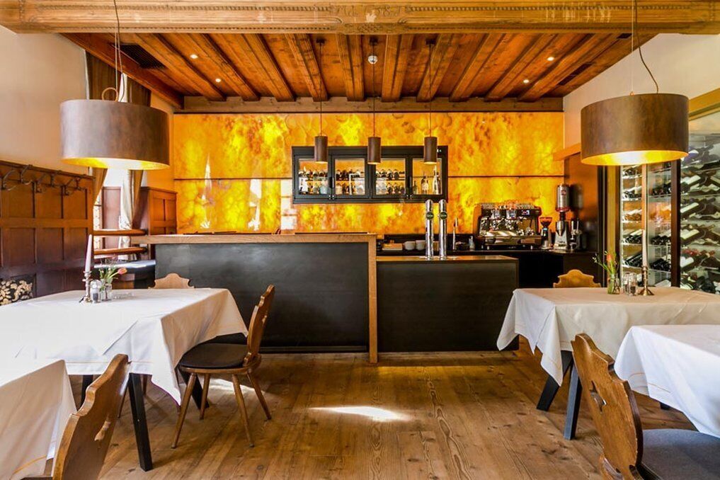 Um restaurante com vigas de madeira no teto, um espaço de bar com prateleiras de garrafas e mesas com cadeiras.