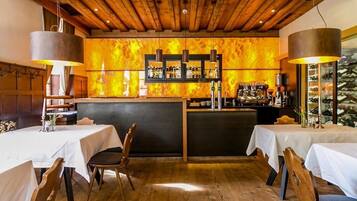 Um restaurante com vigas de madeira no teto, um espaço de bar com prateleiras de garrafas e mesas com cadeiras.