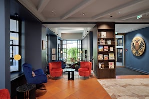 A modern lobby with red and blue chairs, a central table, and a bookshelf. - Hotel Sailer (Innsbruck)