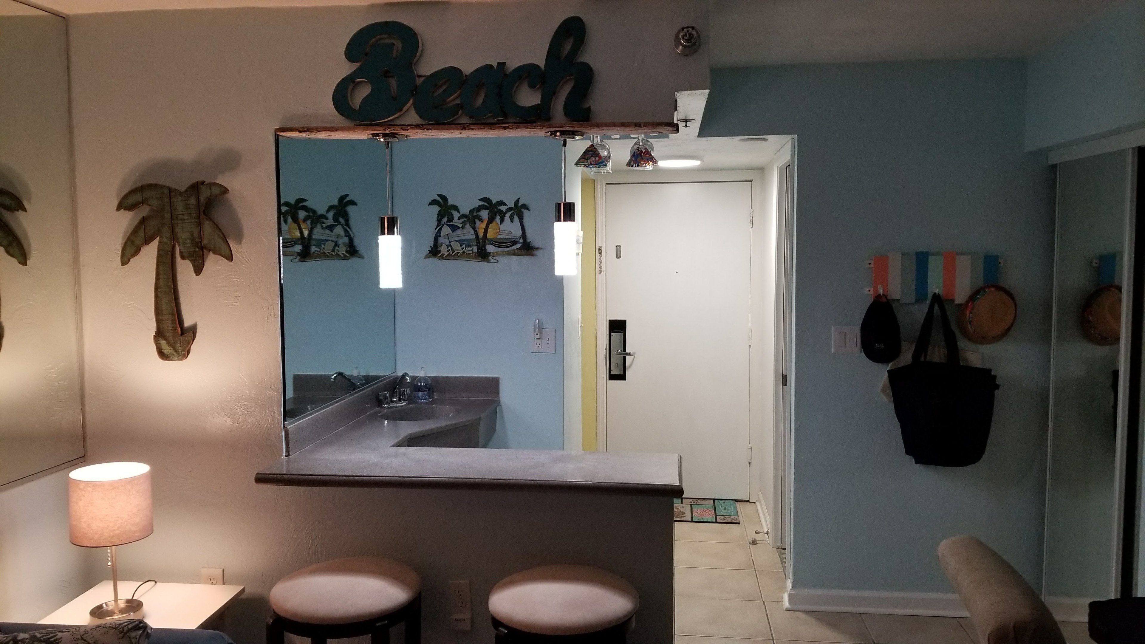 Une salle de bain avec un grand miroir, un lavabo et des toilettes. Un porte-serviettes est fixé au mur, et on y voit une serviette et un sac suspendus.