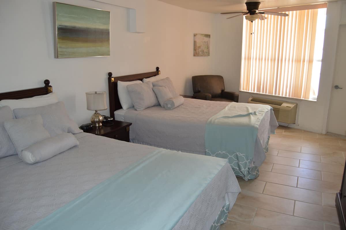 A hotel room with two beds, a ceiling fan, a chair, and a window with blinds.