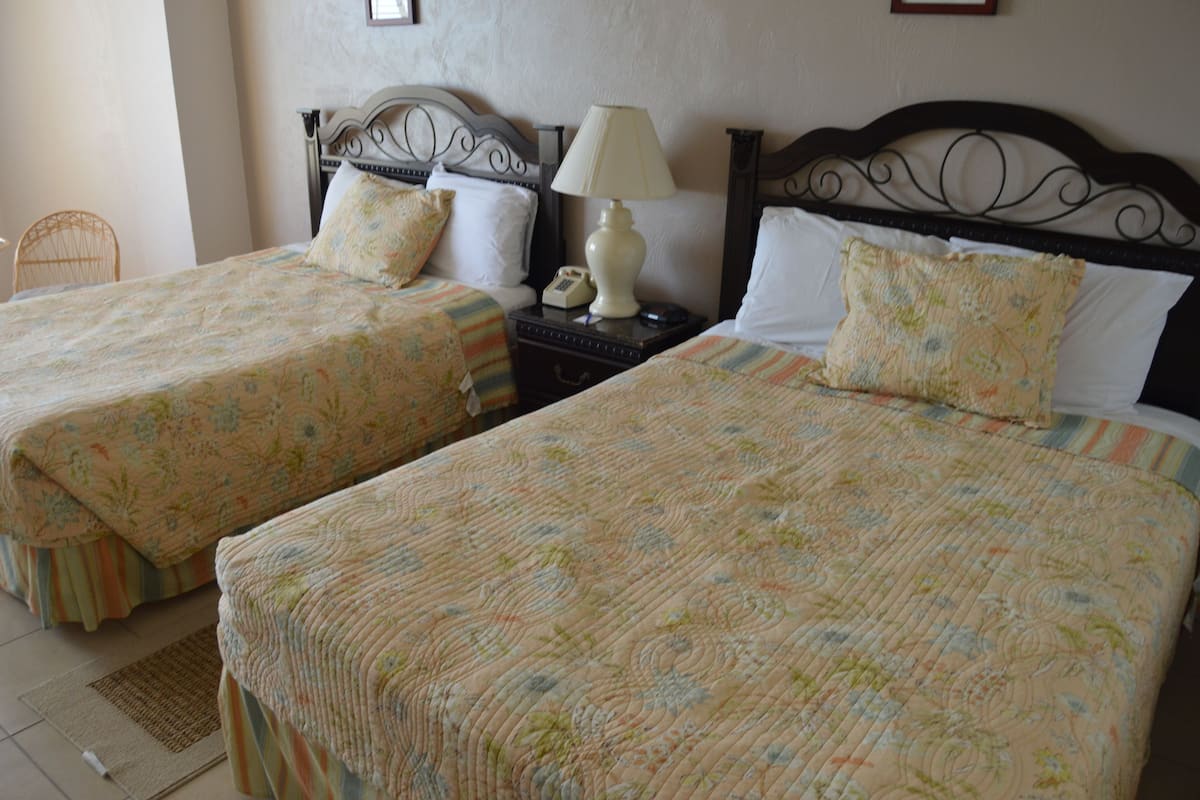A hotel room with two beds, each with floral bedding and a headboard. There is a bedside table with a lamp and a telephone.