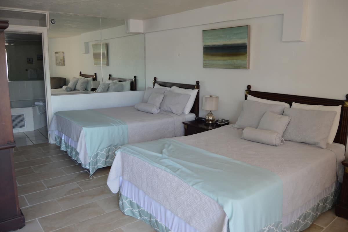 A hotel room with two beds, a large mirror, and a painting on the wall.