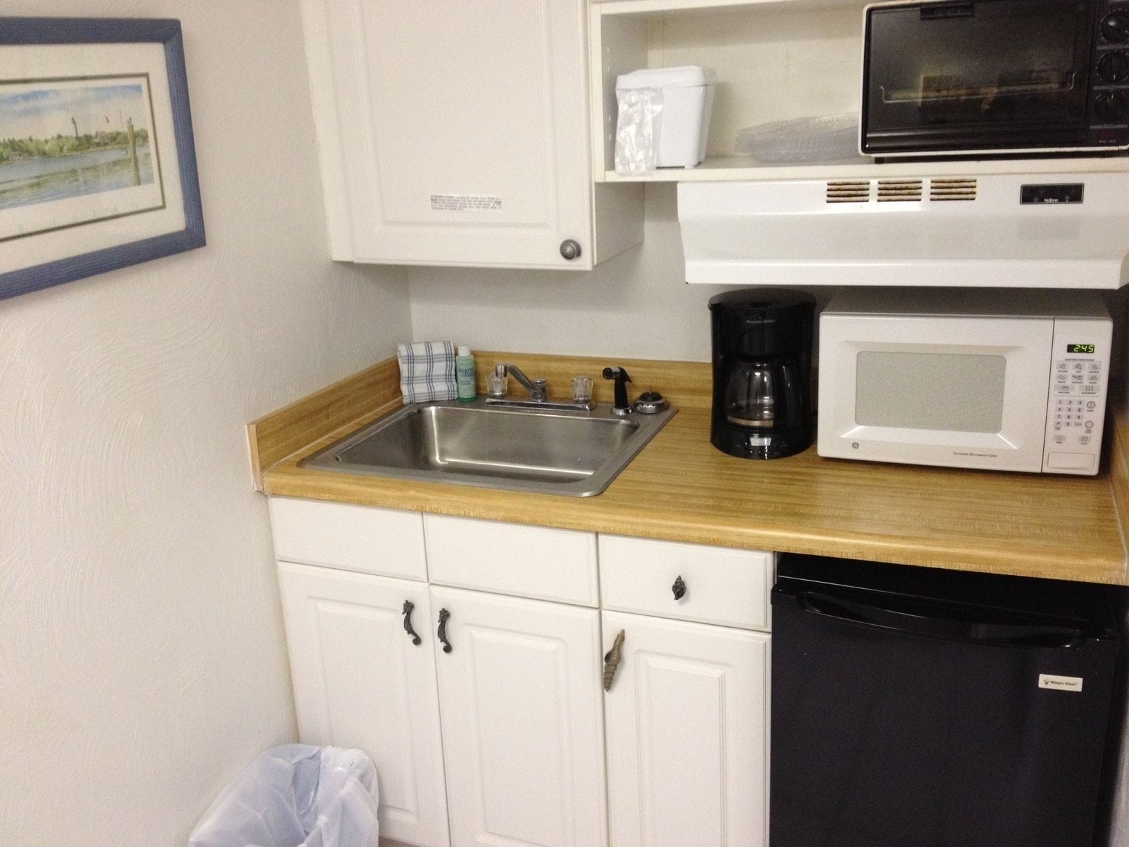 A compact kitchen with a sink, a coffee maker, a microwave, and a dishwasher.