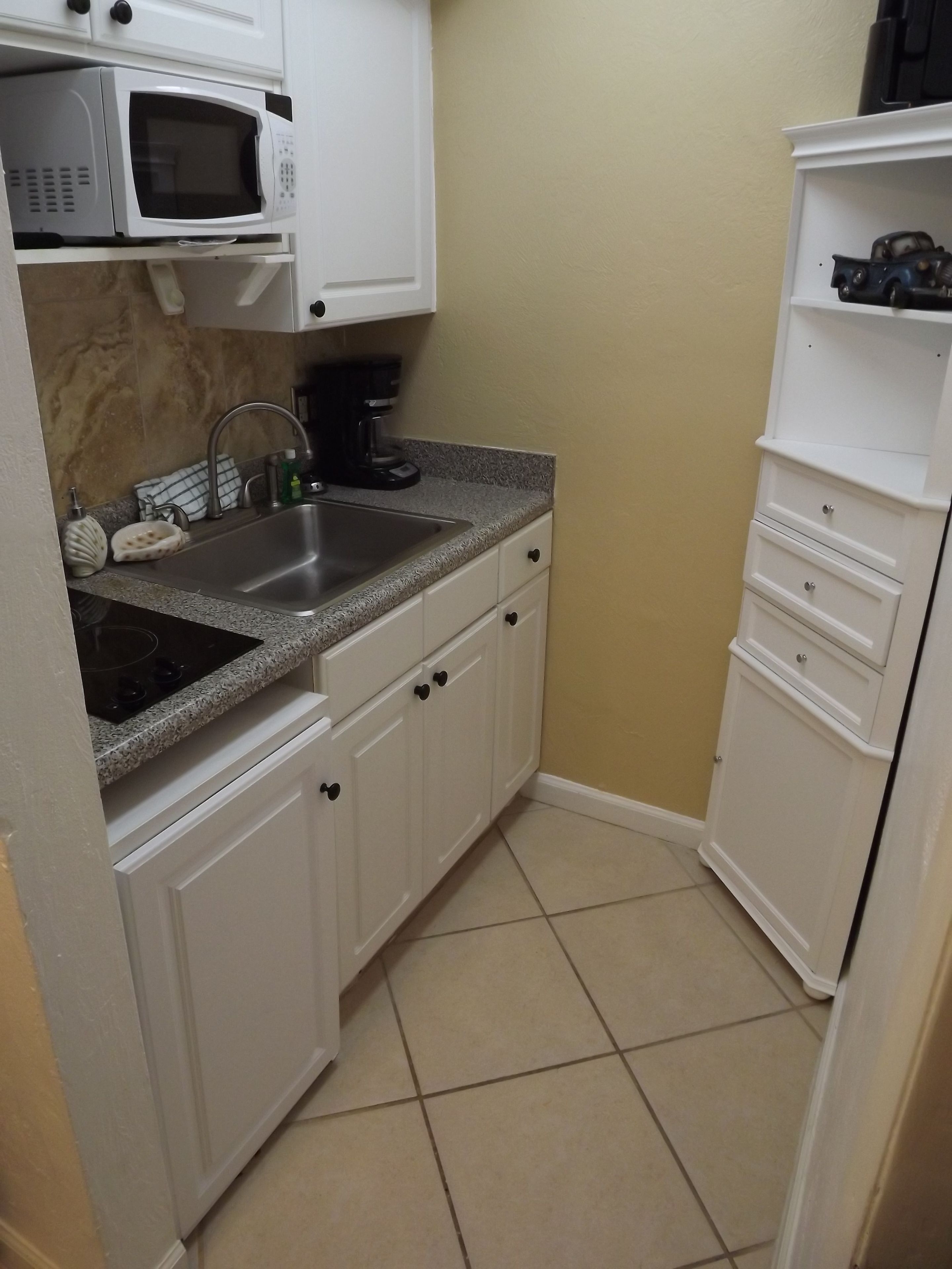 A compact kitchen with white cabinets, a granite countertop, a sink, a microwave, and a coffee maker.