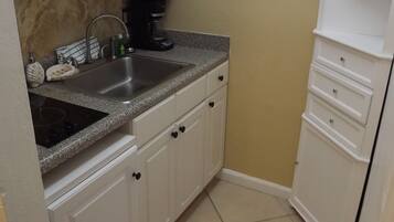 A compact kitchen with white cabinets, a granite countertop, a sink, a microwave, and a coffee maker.