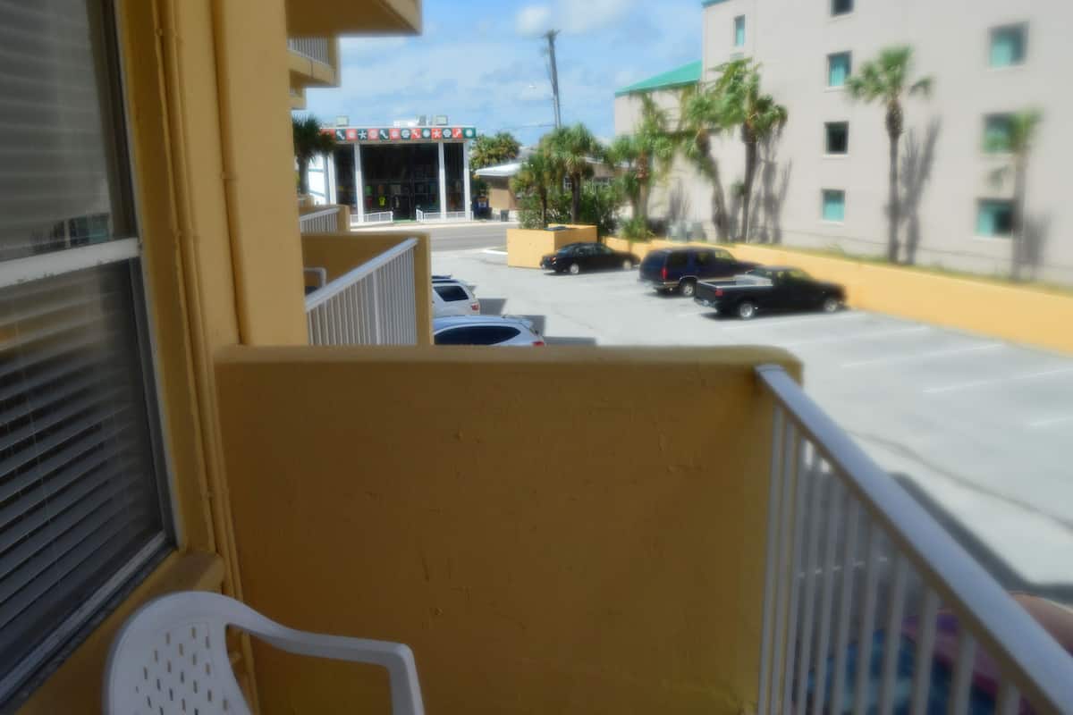 A view from a balcony overlooking a parking lot with several cars, a building with a sign, and palm trees.