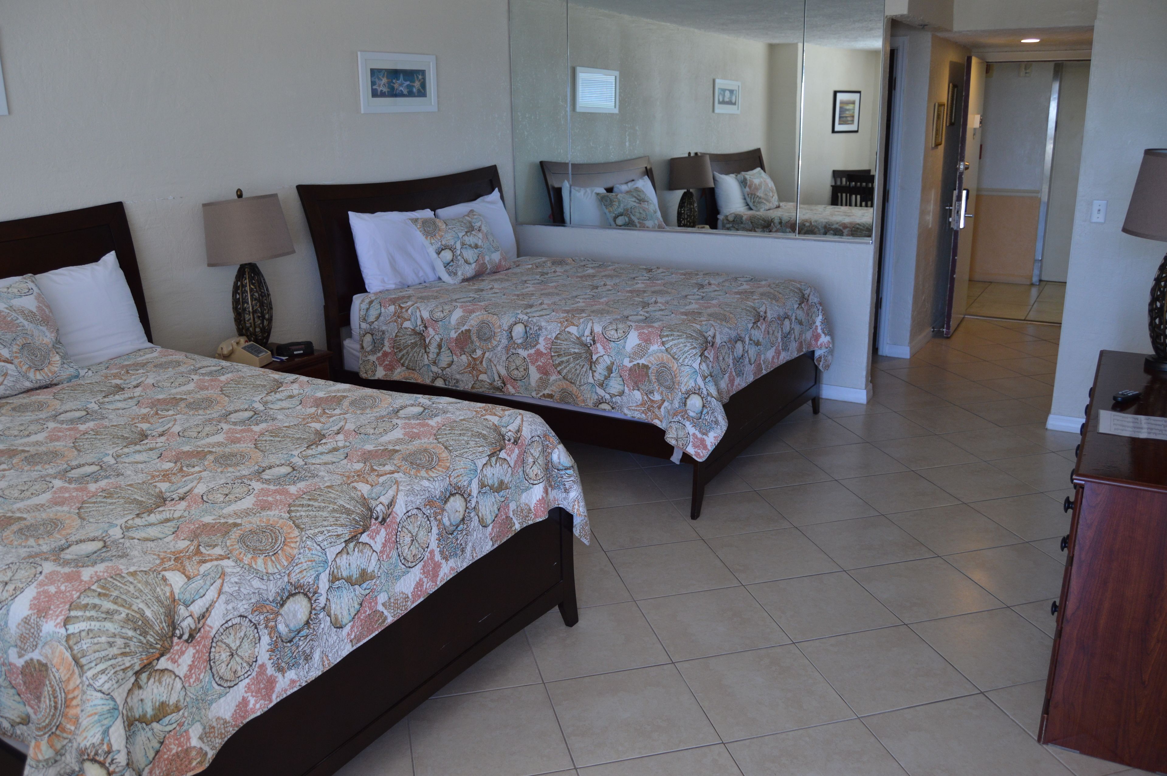 A hotel room with two beds, a mirror, a desk, and a wardrobe.