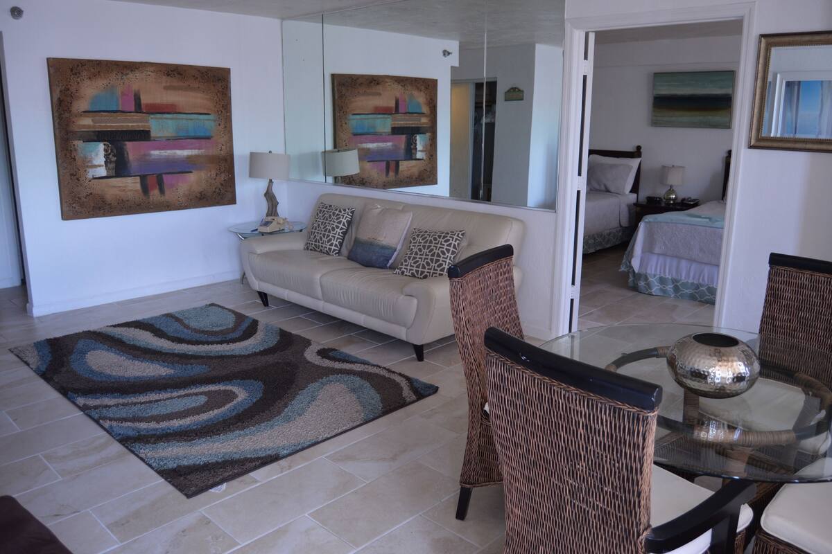 A modern living room with a sofa, a glass coffee table, and a patterned rug.