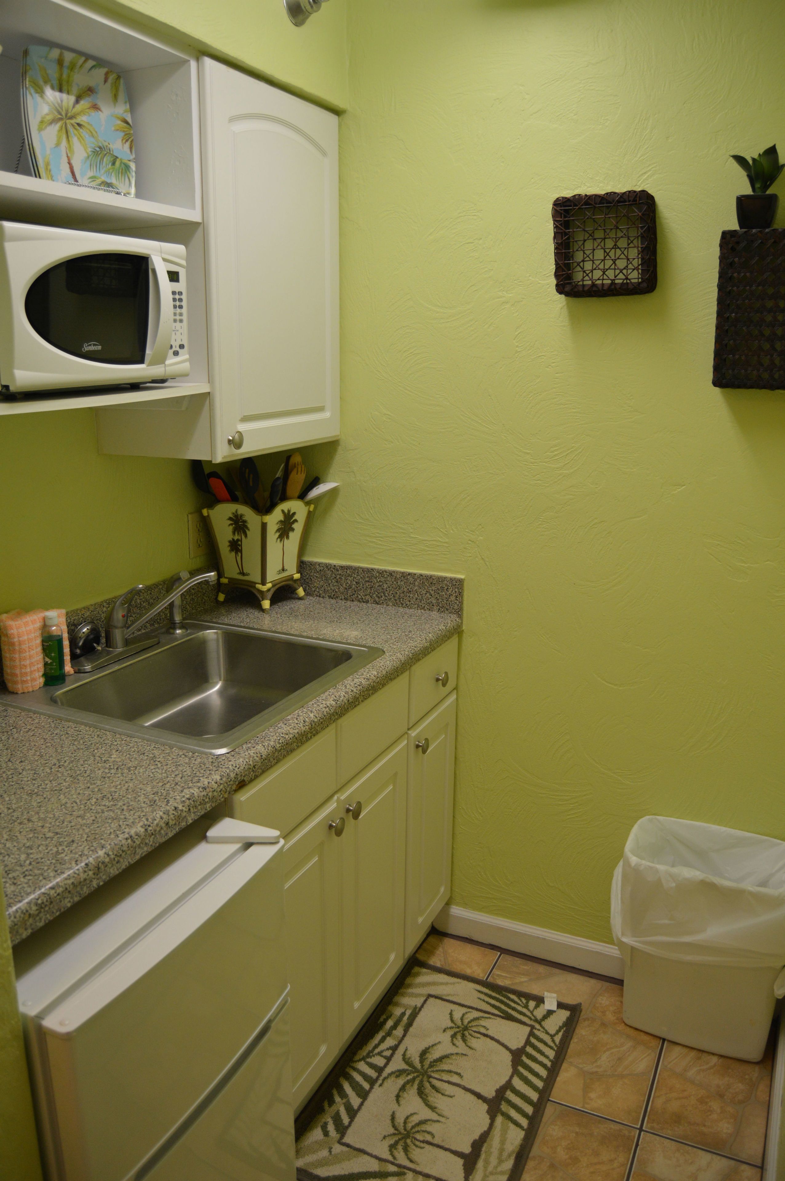 A compact kitchen with a microwave, sink, and a small trash bin.