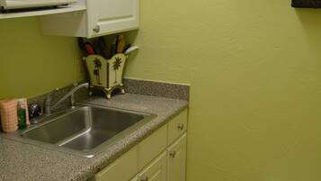 A compact kitchen with a microwave, sink, and a small trash bin.