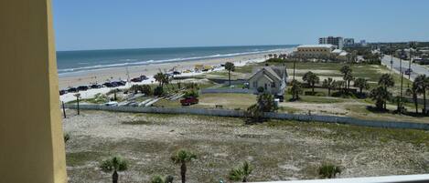 A beach view with a building, palm trees, and a clear sky.