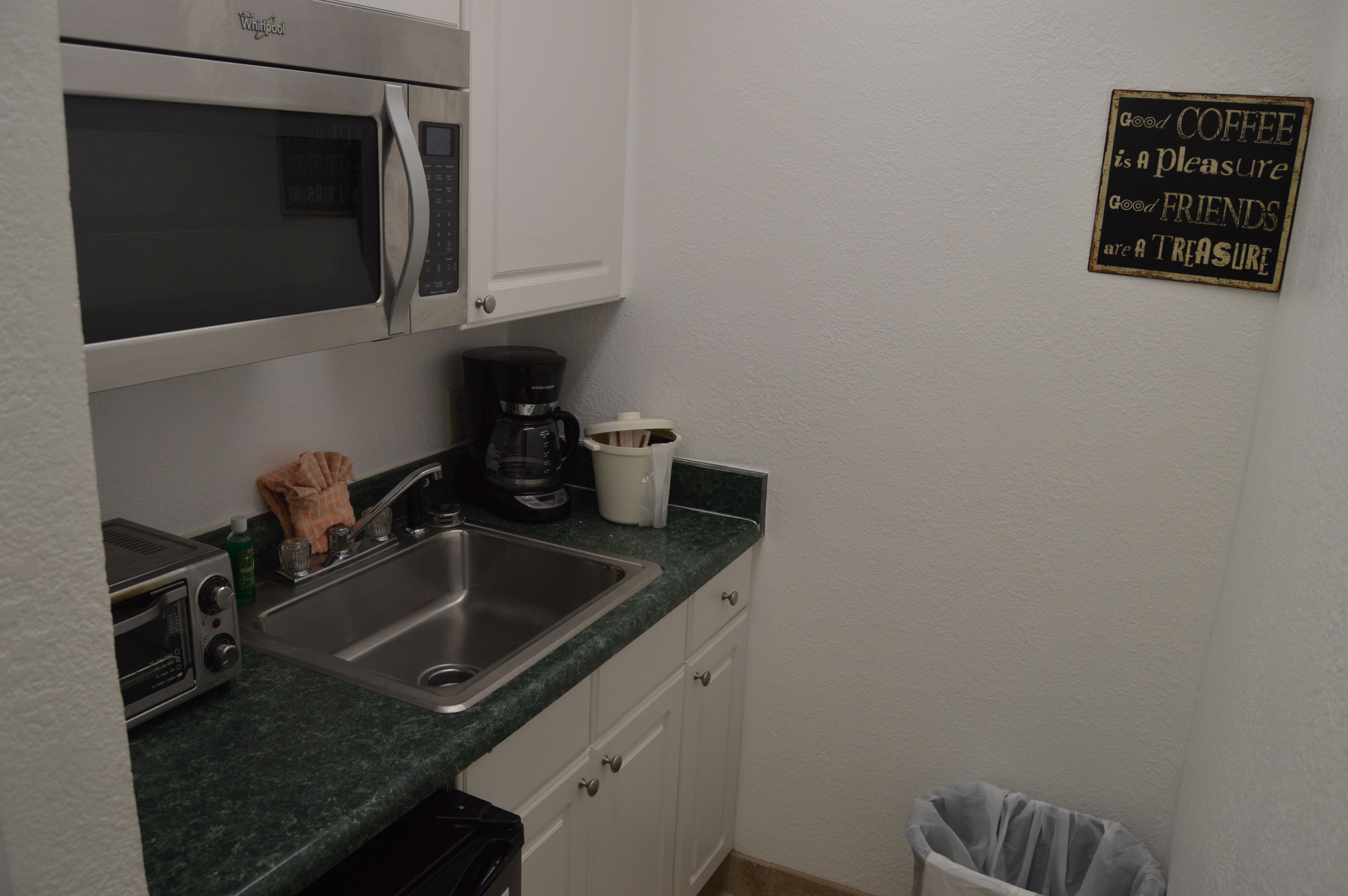 A compact kitchen with a microwave, toaster, sink, and coffee maker.