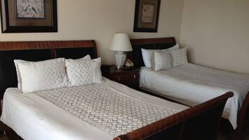 A hotel room with two single beds, a nightstand with a lamp, and two framed pictures on the wall.