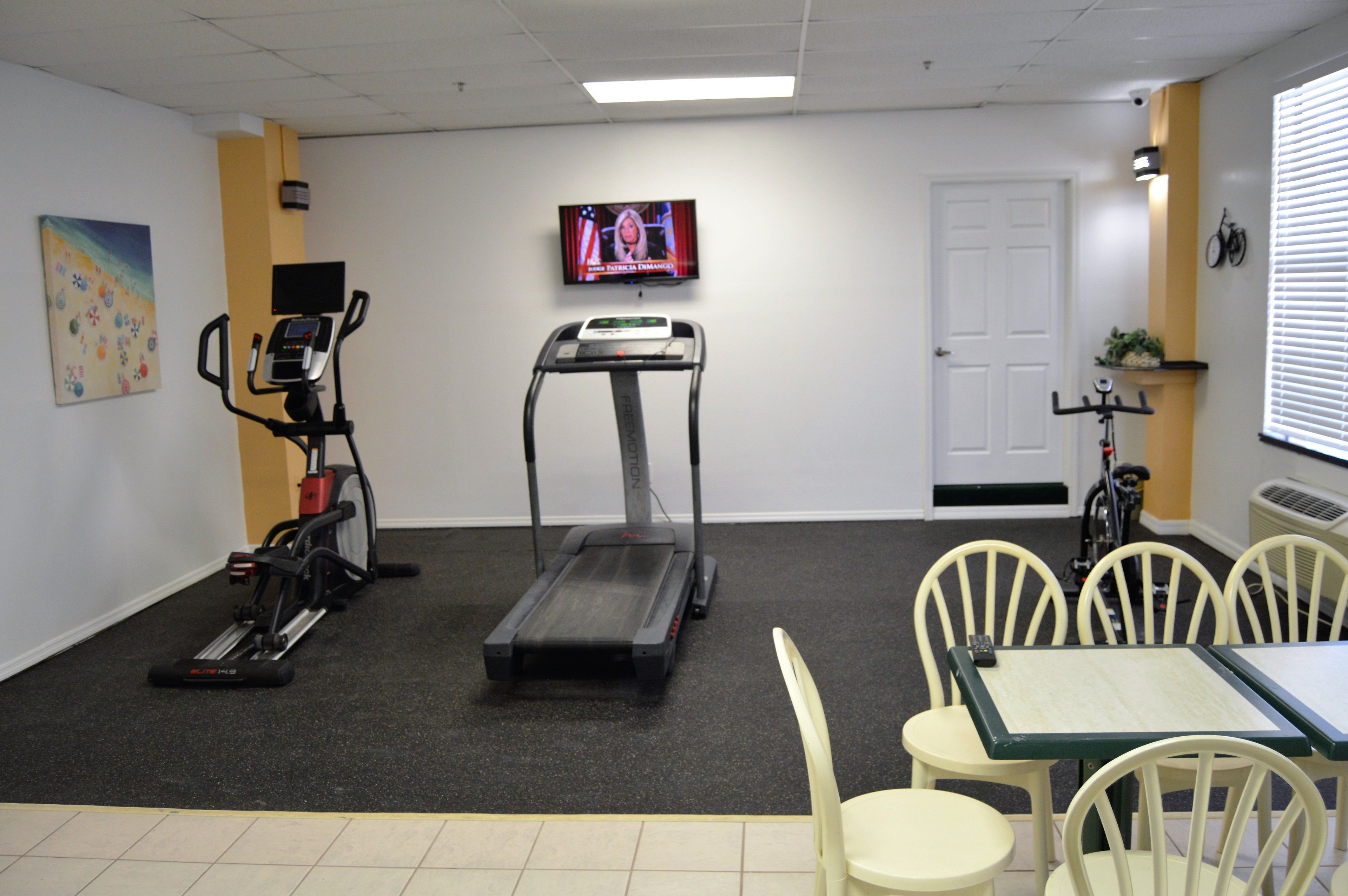 A fitness room with exercise equipment, a television, and a table with chairs.