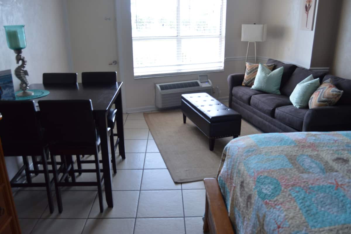 A room with a dining table, chairs, a sofa, a coffee table, and a bed.