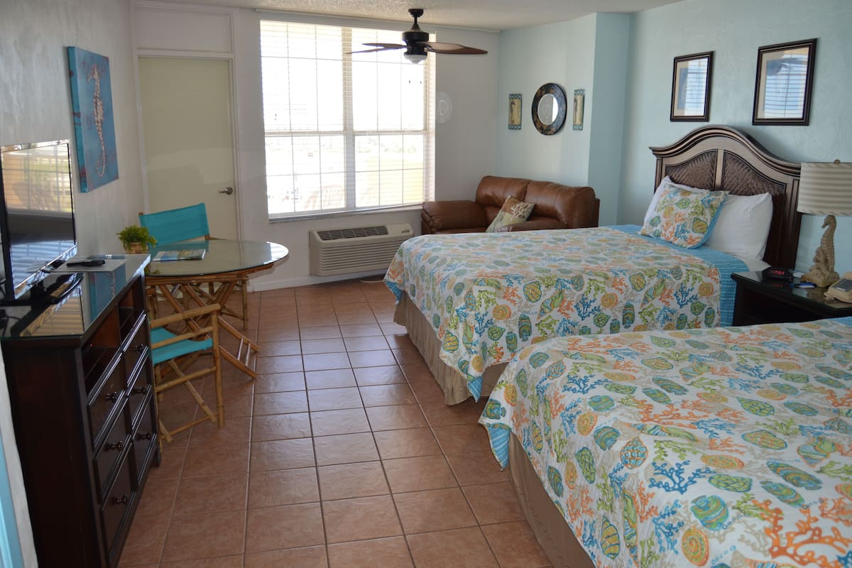 A bedroom with two beds, a desk, a chair, a ceiling fan, and a window.