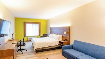 Habitación de hotel con cama, escritorio, silla, sofá, televisión y ventana.