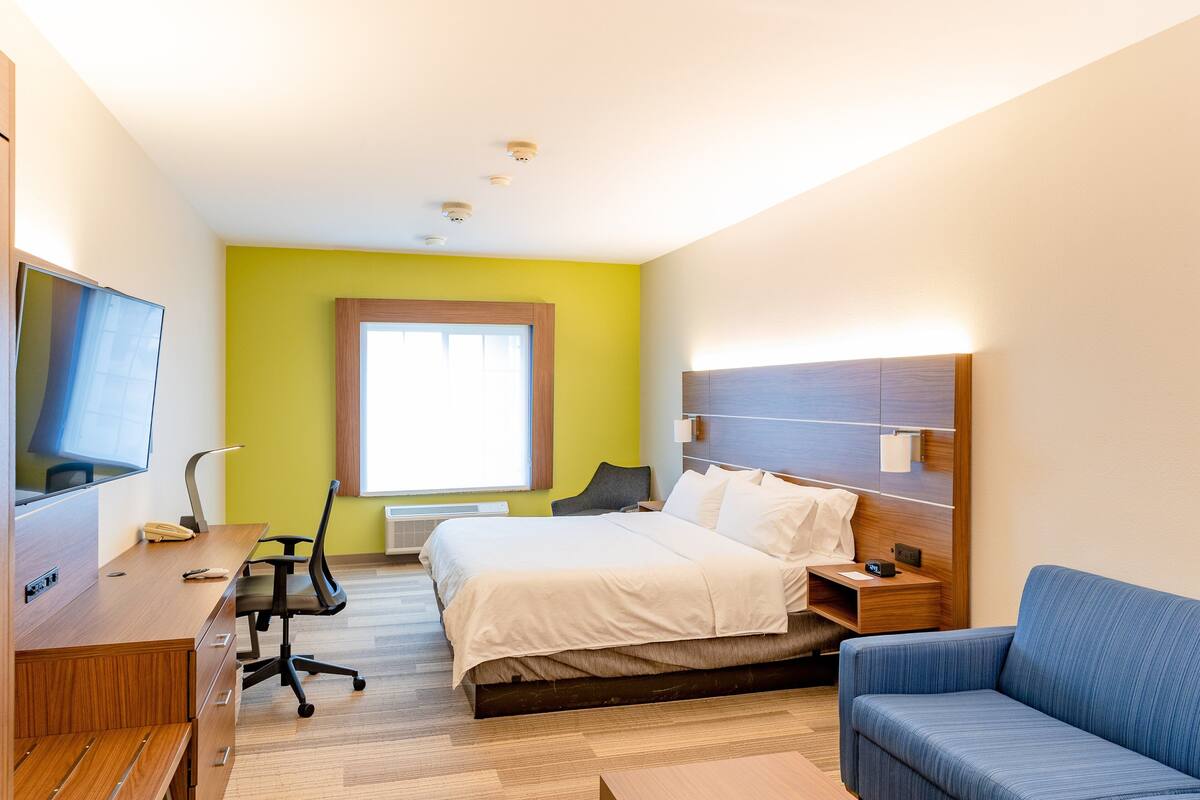 A hotel room with a bed, a desk, a chair, a TV, and a window.